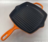 Top angle view of square orange cast iron grill skillet with ridged interior surface and handles.
