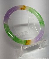 Natural round jade bangle showing its multicolor glaze and polished finish on display stand.