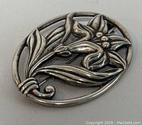 Front view of an oval sterling silver floral brooch with detailed flower and leaf design.