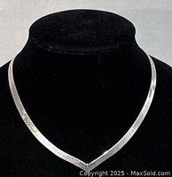 Front view of the flat V-shaped silver necklace displayed on a black bust to highlight the shape and texture.