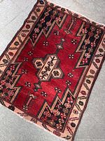Full view of the vintage hand-woven wool rug placed on the floor, showing the red geometric pattern with cream and black borders.