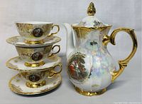Stacked teacups on saucers showing gold trim, decorative scenes on porcelain.