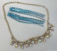 Blue rhinestone earrings laid flat next to clear rhinestone collar necklace showing size and detail.
