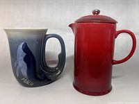 Side-by-side view of vintage Maui whale mug and red Le Creuset French press on white background
