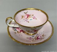 Full view of teacup and saucer set with hand painted floral designs and gold trim.