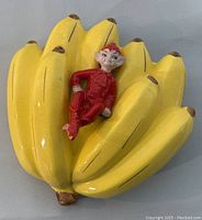 Front view of yellow ceramic wall hanging planter in the shape of bananas with a red pixie figure.