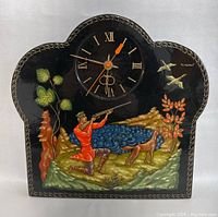 Front view of the wall clock showing detailed hunting scene painting and clock face with Roman numerals and orange hands.