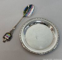 Silver round dish and colorful enamel spoon set on grey background, showing entire set