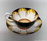 Angled view of the teacup resting inside the matching saucer showing interior floral design and gold trim around scalloped edges.