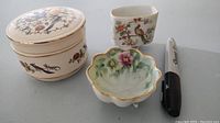 Three footed ceramic pieces arranged with marker for size comparison. Includes Nippon trinket box, Sadler footed bowl, and small ceramic cup with bird design.