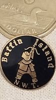 Front view of round enamel pin showing black background with gold-colored Inuit hunter figure and text 'Baffin Island N.W.T.'