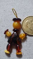 Close-up image of a small Baltic amber figure made of multiple colored amber beads strung together, next to a coin for scale.