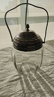 Front view of the biscuit jar with the lid closed, showing clear faceted glass body and silver plated lid and handle.
