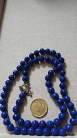 Full view of the blue bead necklace laid out showing bead size relative to a coin.