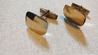 Pair of gold-toned cufflinks lying on fabric showing the front and T-bar sides.