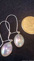 Pair of pearl drop earrings with silver wire hooks placed beside a Canadian quarter for scale, showing size and design details.