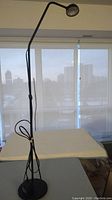 Full view of black metal floor lamp on table by window, showing height and design.