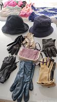 Photo showing two fabric hats, six pairs of gloves in different colors and styles, and a small mauve purse with purple strap.
