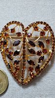 Close-up photo of the heart-shaped brooch showing intricate gold tone metalwork and amber stones with a coin for size comparison.