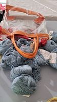 Close-up of clear plastic bag with brown leather handles on light blue knitted fabric and yarn skeins showing contents of the lot.