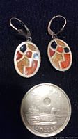Pair of oval earrings with gold tone metal and enamel inlays in black, red, yellow, and amber colors next to a Canadian dollar coin for scale.