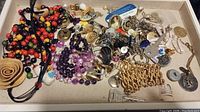 Overview photo showing assorted costume jewelry and decorative pieces spread out in a box, including colorful bead strings, metal pins, a gold-tone bracelet, and various pendants.