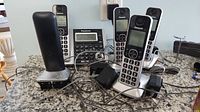 Five Panasonic cordless phones with charging cradles on granite countertop with power adapter cables.