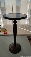 Full view of the pedestal table showing dark metal base with vertical decorative design and round stone top