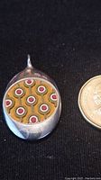 Front of pendant showing mustard yellow fabric insert with circular pink and white pattern, next to coin for scale.