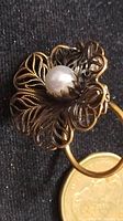 Close-up front view of scarf clip showing filigree flower design with faux pearl center and part of a coin for scale.
