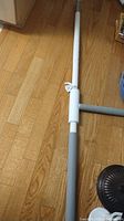Photo displaying full length of the white and gray adjustable security pole lying on a wooden floor showing different segments and grips