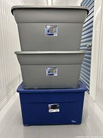 Stacked view of two gray totes on top of one blue tote inside a storage unit.