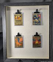 Full view of the display frame showing four Charizard gold foil fan art cards in individual protective sleeves clipped to textured backing, framed in dark wood with gold trim.