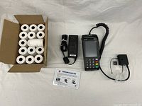 Full lot showing debit card machine, power adapter, box of receipt paper rolls, single extra roll, and cleaning card