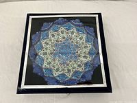 Closed display case showing the Mina enamel plate's top geometric design with blue, white, and brown floral enamel patterns.