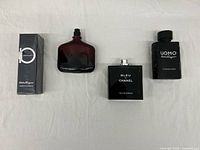 Fragrance lot with four bottles/items on white cloth background showing sealed boxed shampoo & shower gel, Uomo cologne, Bleu de Chanel, and Uomo Signature bottle.
