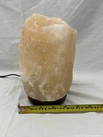 Natural Himalayan salt lamp with measuring tape showing about 7 inch height and 4 inch width.
