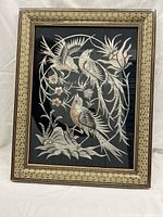 Front angled view showing the metal artwork of birds and flowers inside an intricately patterned inlay wooden frame.