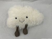 Front view of the plush cloud toy showing its fluffy cream fabric, black shiny eyes, stitched smile, and grey corduroy feet.