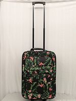 Full front view of Jetstream carry-on suitcase with extended telescopic handle and two wheels visible at base. Black fabric with vibrant tropical floral design and two front zippered pockets.