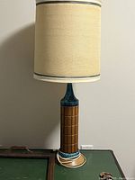 Ceramic base lamp with blue and brown geometric design and beige drum shade with grey trim.