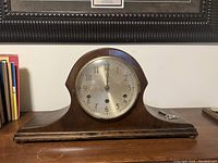 Front view of antique mantel clock with round metal face and glass cover, clock key placed next to clock on wooden surface.