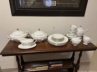 Full view of Minton bone china set laid out on table showing 2 soup tureens, stacked plates, 5 teacups with saucers, teapot, milk jug, sugar bowl, and gravy boat with attached plate.