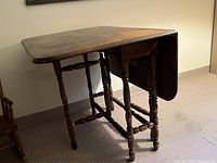 Photo of antique wooden drop leaf table showing both leaves extended, turned legs, wear, and overall condition.