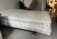 Photo of full bed setup including metal frame with caster wheels, boxspring, and mattress with floral pattern fabric