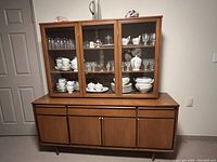 Front view of 1970s style china cabinet with glass doors and wooden base, shelving visible inside
