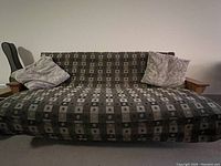 Wood frame futon visible with mattress covered in a patterned fabric and two large cushions on either side