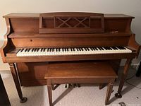 Front view of Willis upright piano with keys and music stand visible, bench included in front.
