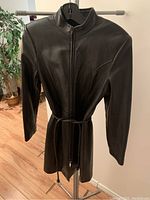 Front view of black leather women's coat with zipper and belt, showing dramatic cut and smooth leather texture