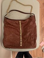 Full view of brown croc embossed leather purse with gold-tone pyramid studs centered on front and leather strap connected to gold chain strap.